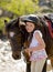 Young girl 7 or 8 years old holding bridle of little pony horse smiling happy wearing safety jockey helmet in summer holiday