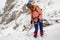 Young girl abseiling a steep rock into a narrow couloir covered in fresh snow, using a tube belay plate, backed up with a prusik