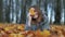 A young girl in an autumn park lies on the leaves and smiles with a leaf in her hand.