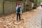 A young girl with backpack kicks autumn leaves while walking along a tree lined path