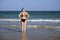 Young girl in a bathing suit and a striped hat is standing in the sea with her hands on her waist. Standing back