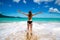 Young girl in bikini with raised arms greeting tropical sea and sun, on beach, freedom, vacation
