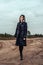 A young girl in a black coat walking on a sandy dirt road under stormy sky