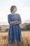 Young girl in blue dress with collected hair poses, looks away in field of ears at sunrise. Foggy dawn in background