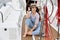 A young girl in a blue striped overalls and a straw hat sits on the deck of a yacht in the azure sea