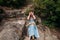 A young girl in a blue sundress sits on the rocks in the mountains and grimaces