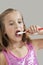 Young girl brushing teeth against gray background