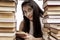 A young girl with a bunch of books sits at the table. Smiling brunette wearing glasses. Back to school. Knowledge and education.