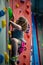 Young girl climbing up on practice wall in indoor rock gym