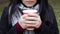 A young girl in a coat holds morning coffee with her while walking in the park. Hand holding paper cup of coffee in green park.