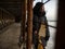 Young girl in a coat stands near metal rusty structures near the sea coast