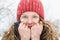 A young girl in a coral-colored hat is holding a collar in her hands to make it warmer, and is smiling under soft fluffy snow