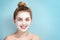 Young girl in a cosmetic mask of white smiling face. Skincare. Blonde woman smiling on blue background. moisturizer mask