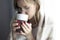 Young girl covered with a blanket, holds a cup in her hands and drinks tea, she gets sick and is treated at home, close-up