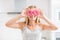 Young girl covered her face with pink donuts in home kitchen. Emotion morning at breakfast