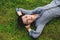 A young girl with dark short hair is lying on the green grass, with hands under her head