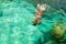 Young girl with diving mask and snorkel dives in clear blue sea water, adult woman in white bikini swims in turquoise clean water