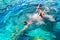 Young girl with diving mask and snorkel dives in clear blue sea water, adult woman in white bikini swims in turquoise clean water