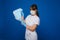 A young girl doctor in a medical mask holds a lot of masks in her hands. A nurse poses on a blue background