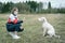 A young girl and a dog in medical masks play in nature.