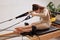 A young girl is doing Pilates on a reformer bed in a bright studio. A slender brunette in a beige bodysuit does