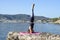 Young girl doing yoga on a small beach pier with a Mediterranean coastal town in the background. Staying fit. Salamba Sirsasana