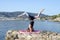 Young girl doing yoga on a small beach pier with a Mediterranean coastal town in the background. Staying fit. Salamba Sirsasana