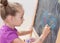Young girl drawing a picture with a chalk on blackboard