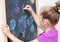 Young girl drawing a picture with a chalk on blackboard