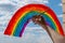 A young girl draws a rainbow on the window glass with a brush and gouache against a blue sky with white clouds. everything will be