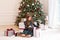 Young girl in dress sit on floor with Xmas gifts in living room. Little girl opening magical christmas present at home. Merry Chri