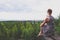 A young girl in a dress sits on a rock ledge above the forest, which is located on the shore of a huge lake.