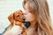 Young girl embraces and kisses a red dachshund puppy on a background of white brick wall