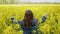 Young girl enjoying nature and sunlight in yellow canola field. She walking forward