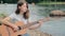 Young girl of European appearance playing an acoustic guitar on the shore of the lake, hobby concept, musical creativity