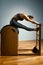 Young girl exercises on a bed of Pilates reformers, in the hall on a background of a gray wall. Fitness stretching