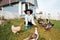 A young girl feeds domestic birds, ducks, hens, geese, turkeys in the yard of a rural house.