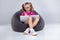 Young girl in glasses doing homework on a gray bean bag