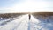 A young girl goes merrily and jumps on a snow-covered field. Winter sunny fun scene with a road and a snowy field