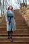 A young girl in gray coat goes down stairs in park on an autumn sunny day