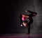 Young girl gymnast in black sport body and uppers standing in bridge pose and holding pink gymnastic ball between leg and neck