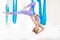 Young girl gymnast in sportswear doing stretching on blue hammock in white studio. Concept aero fly yoga