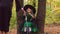 Young girl in Halloween dress upset sitting between two trees and after getting balloons from the woman is very happy.