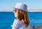 Young girl in a hat and sunglasses stands a back near the sea