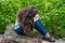 A young girl with her long hair sits in the park with her face covered. The girl is somewhat upset, upset.Maybe crying.