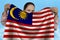 Young girl holding in both hands the national flag of Malaysia on beautiful shiny silk against a blue sky, state concept, travel,