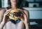 Young girl holding in female hands fast food burger, american unhealthy calories meal on blue background, mockup with copy space