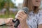 Young girl holding mic with two hands. Microphone and girl singer close up. Cropped image of female teen singer in park