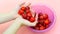 A young girl holds a strawberry in her hands against the background of strawberries in a plate. Red, ripe berry in the hands. Pink