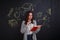 Young girl, with interest reads a book, standing next to a whiteboard with a picture of science.